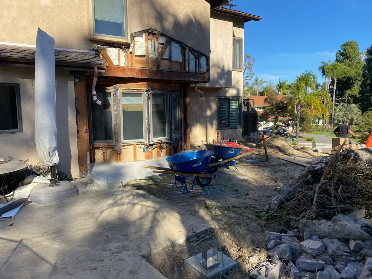 Demolition underway behind the house, where a bay window and dark wood siding sat under two stories of stucco.