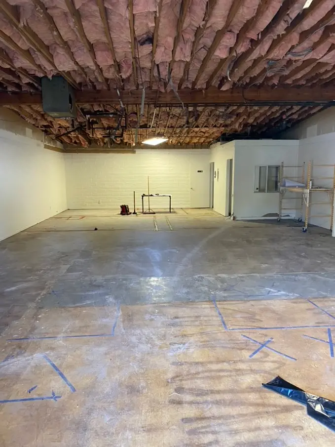 Blue tape marks out the layout on the slab, under joists packed with pink batt insulation, with an existing partition and door opening off to the right.