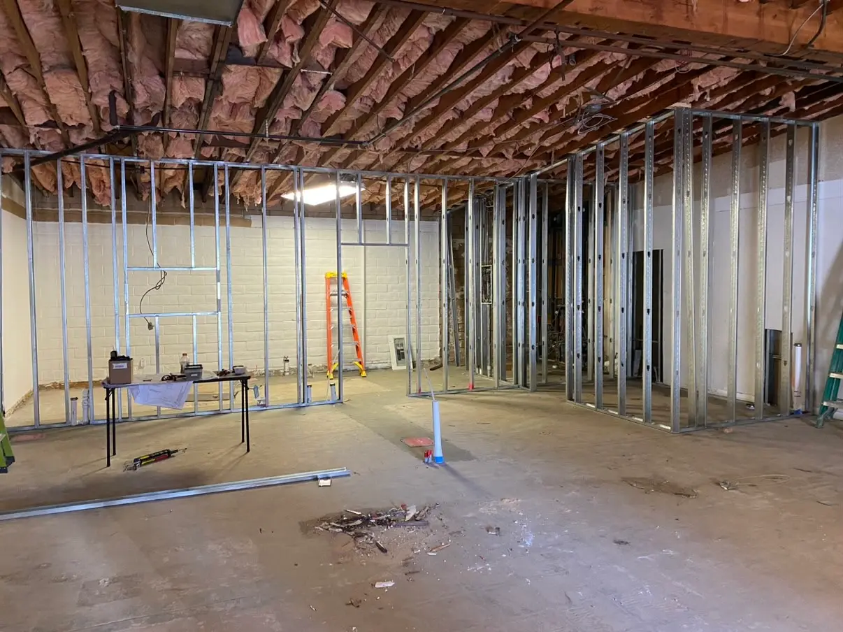 A plumbing riser stands out on the open slab beside a new steel partition running out from the block wall into the middle of the room.