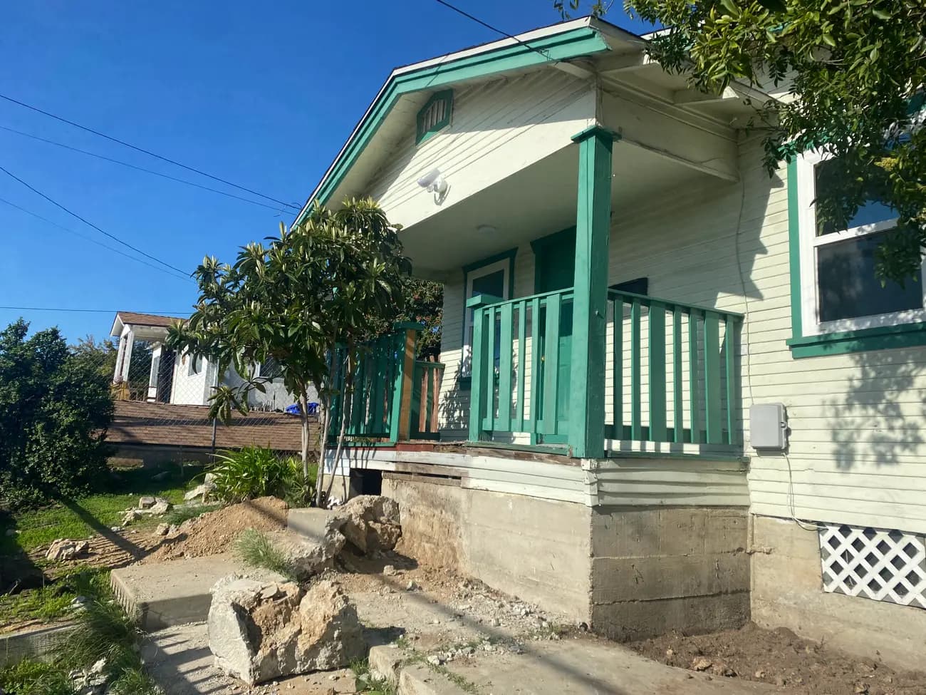 The entry before the work, with the original green railing and the ground already opened along the foundation.