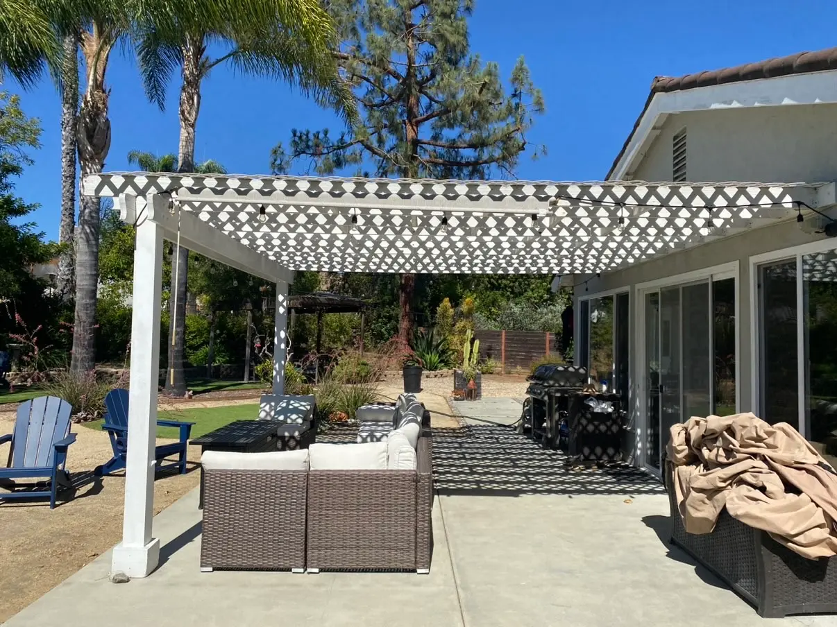 String lights hang under the original open lattice cover, with a wicker sectional and blue Adirondack chairs out on the slab.