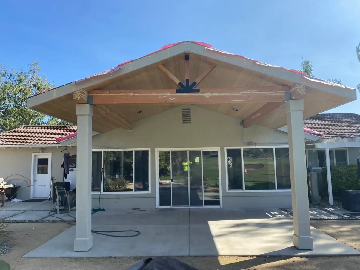 The gable centers over the sliding doors on two white columns, with a hose and a black tarp still out on the patio.