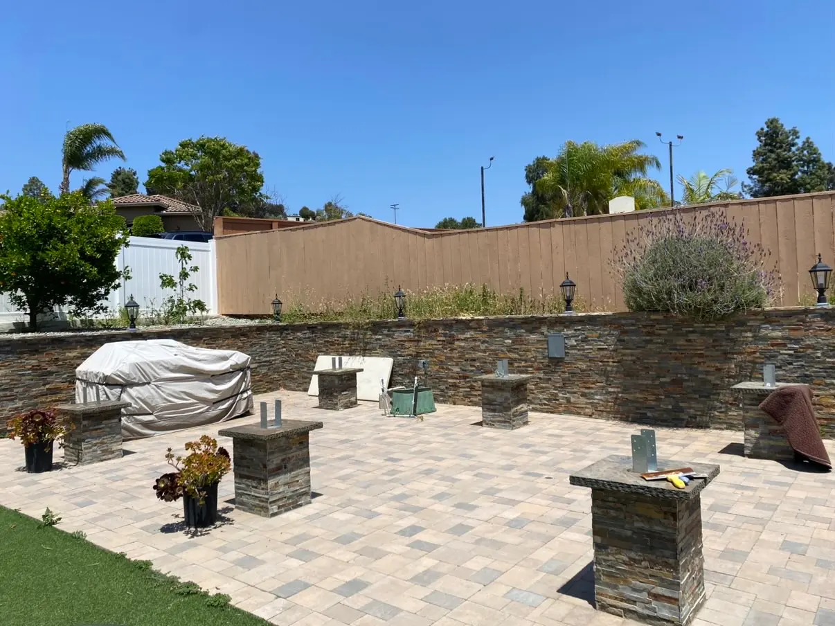 The existing paver patio and stacked stone retaining wall, with the new stone piers built and galvanized post bases set into the pier caps.